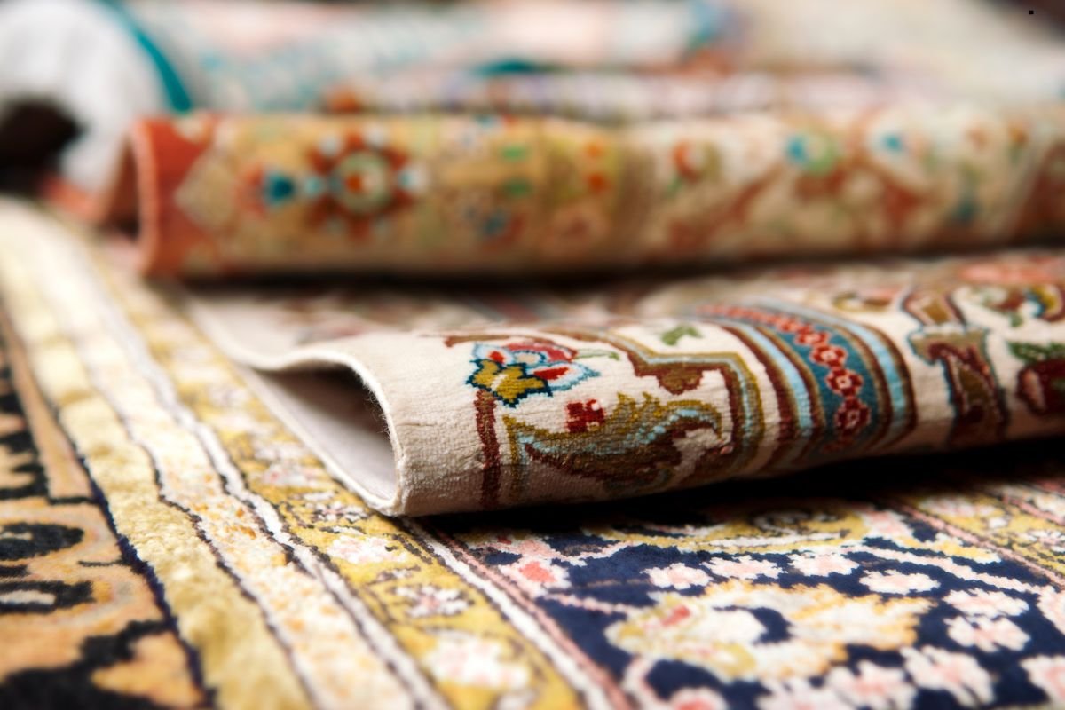 Close-up of intricately patterned and rolled Persian rugs, showing vibrant colors and detailed designs on a soft fabric surface.
